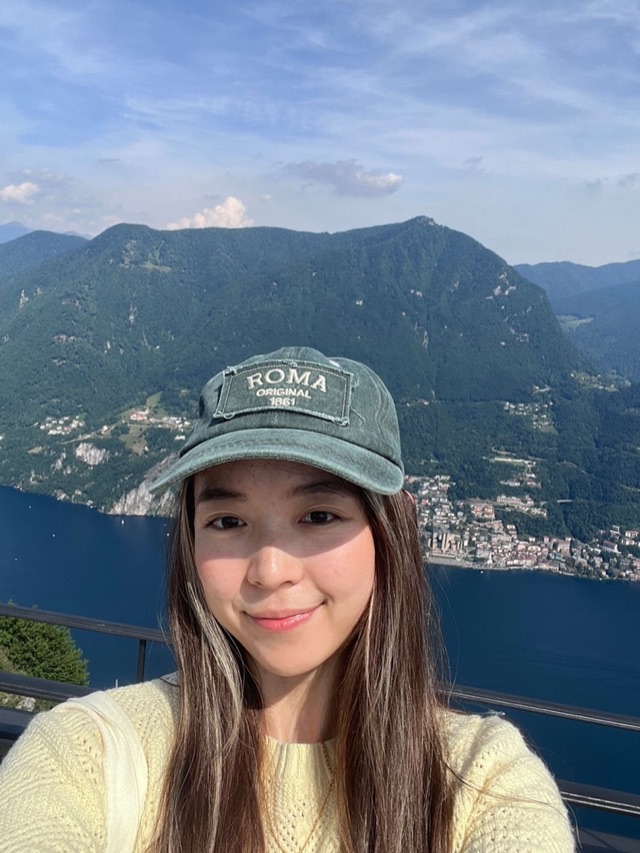 Rebecca smiling in a green cap above a lake and mountains
